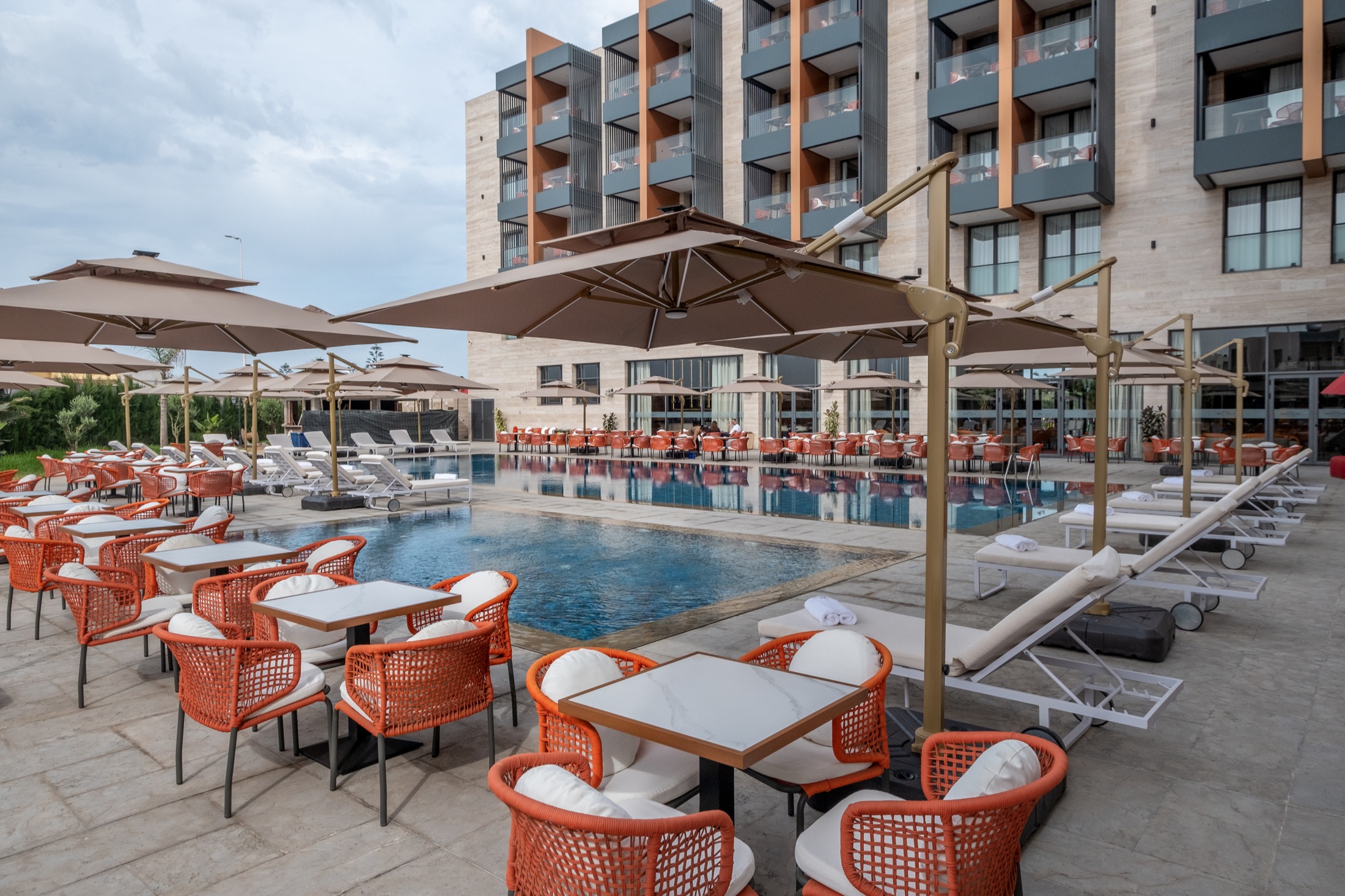 La piscine, ses transats et la façade de l'hôtel sous le ciel bleu
